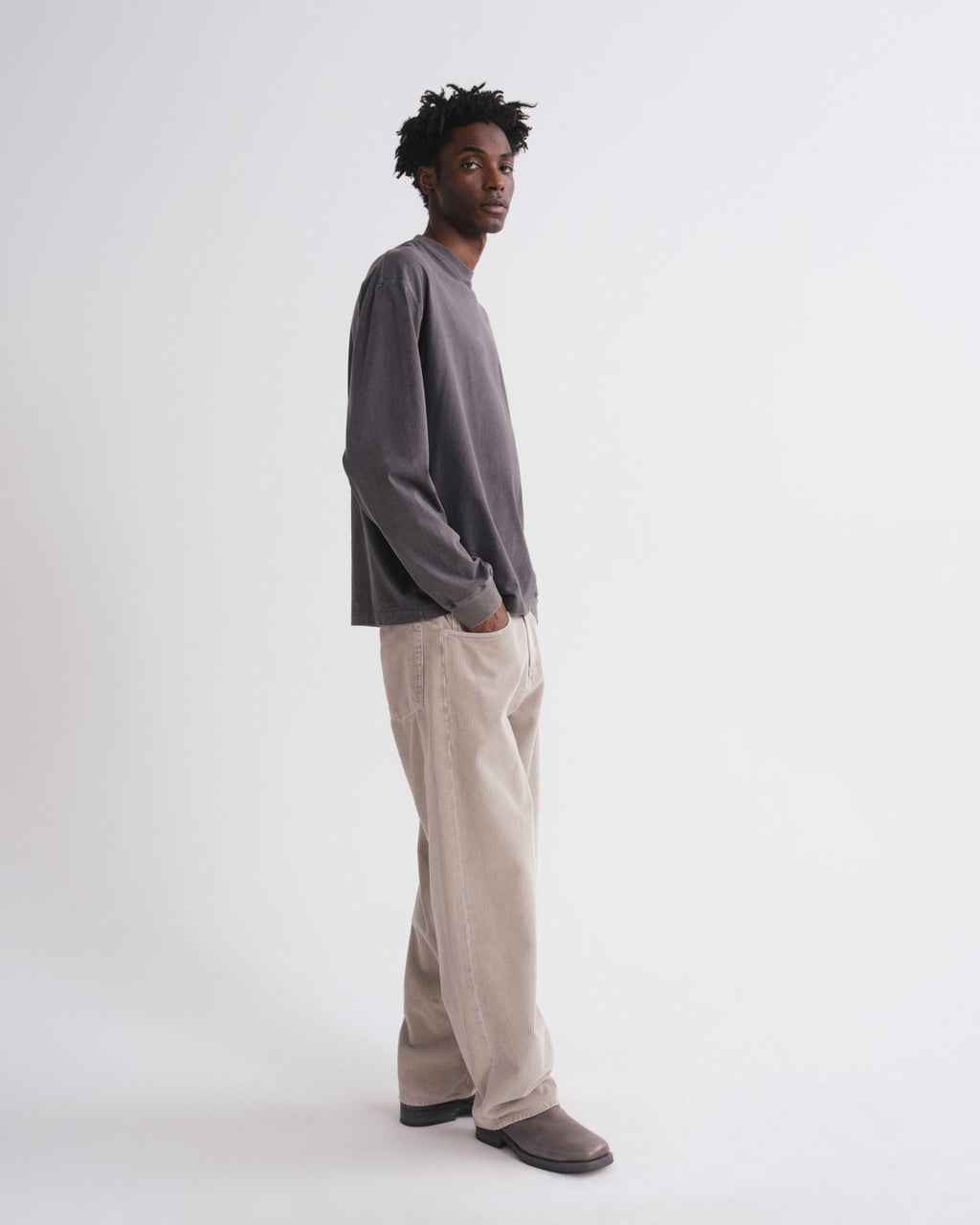 Side view of man wearing a dark grey long-sleeve shirt and beige pants on a grey background