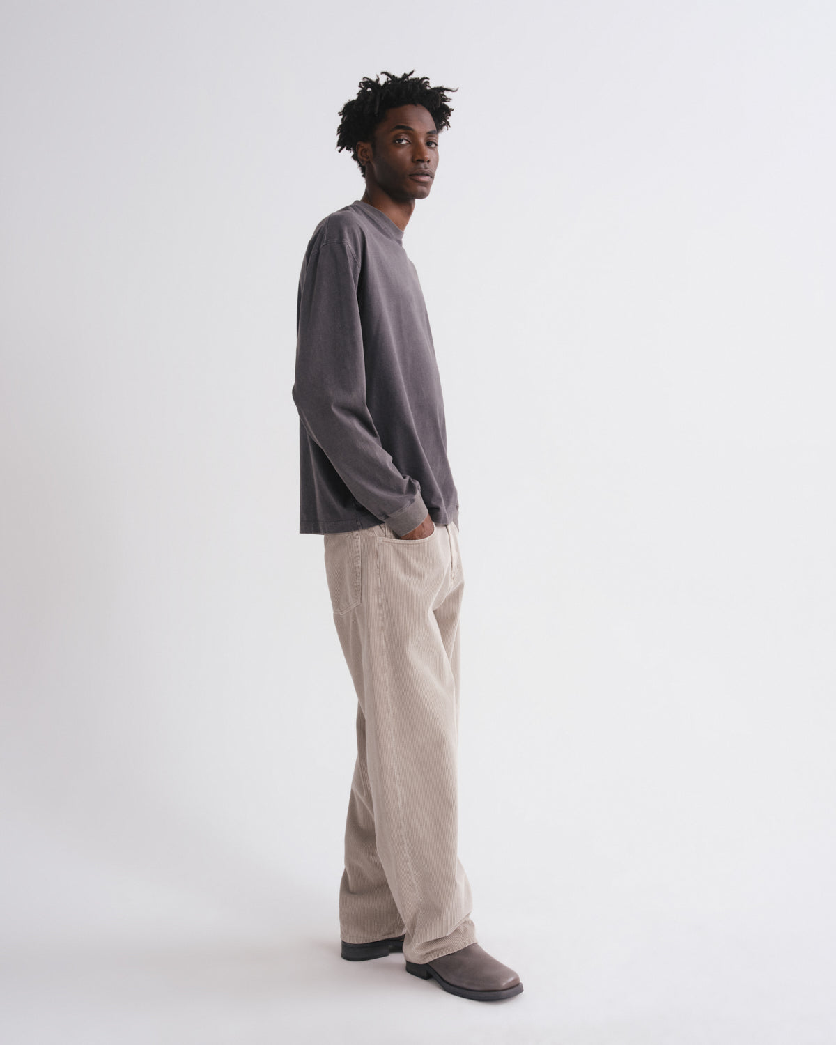 Side view of man wearing a dark grey long-sleeve shirt and beige pants on a grey background