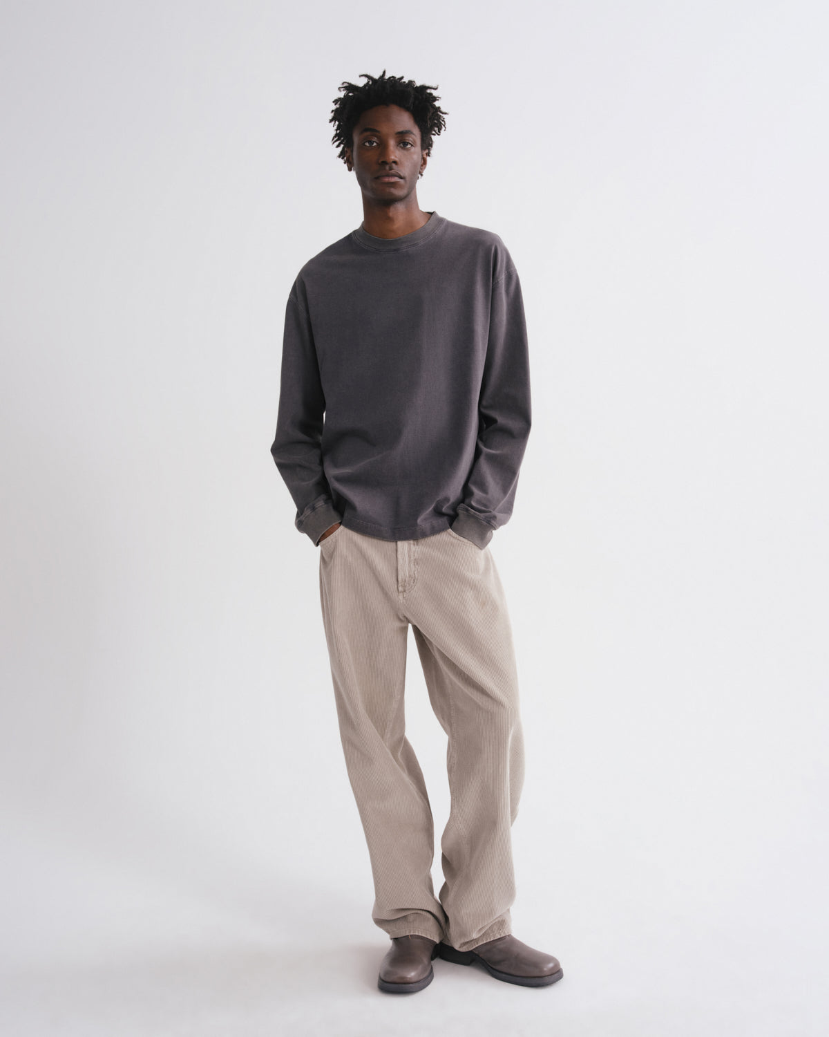 Man wearing a dark grey long-sleeve shirt and beige pants on a grey background