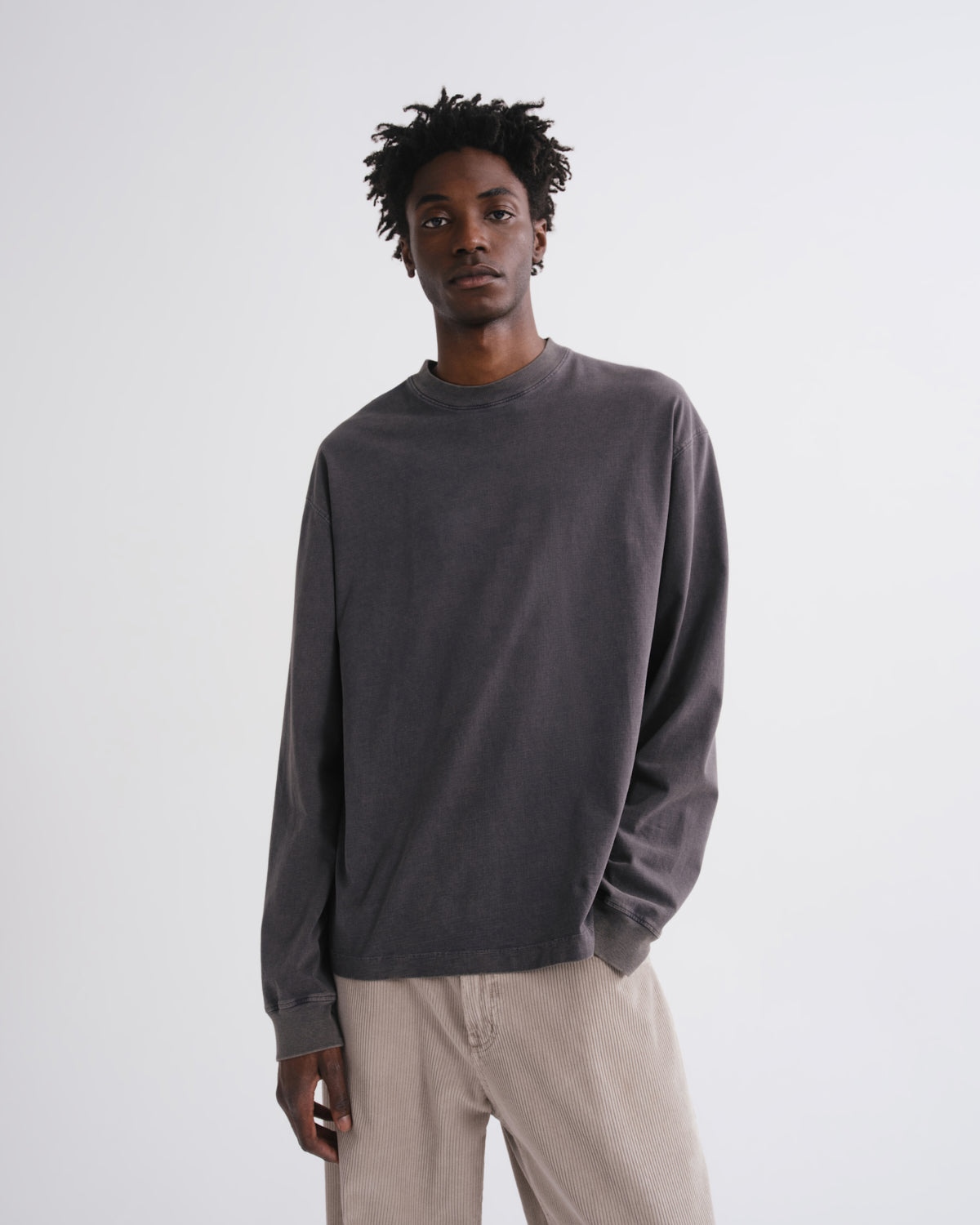 Close up of man wearing a dark grey long-sleeve shirt and beige pants on a grey background