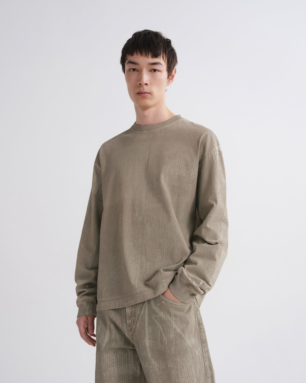 A man wearing a light brown corduroy long-sleeve shirt and matching corduroy pants, standing against a plain light gray background.