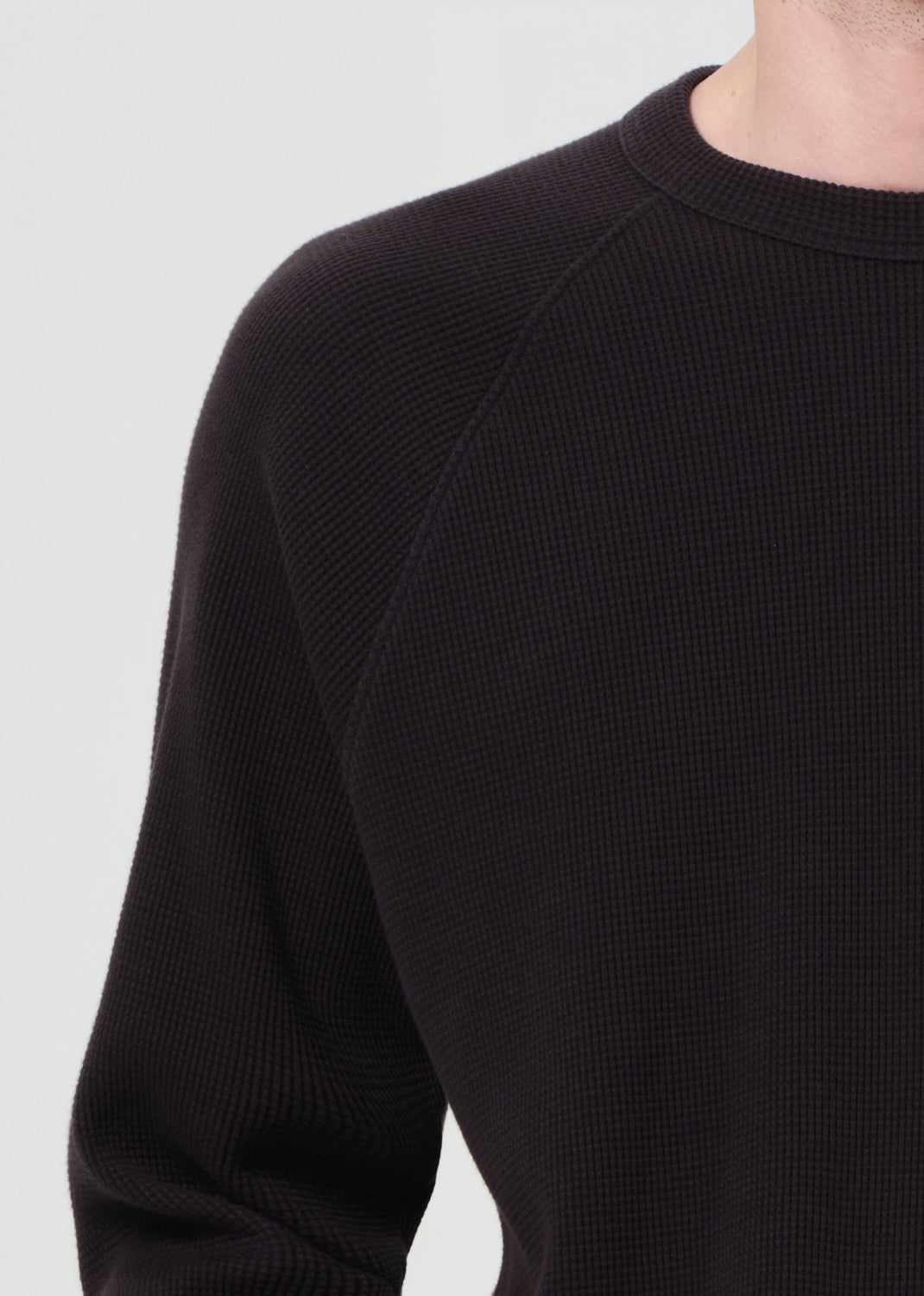 Close-up of a person wearing a black textured sweater against a light background
