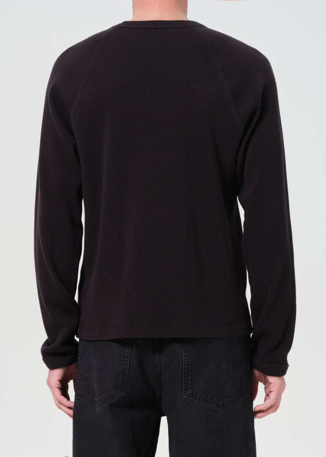 Person wearing a black textured sweater on a plain background