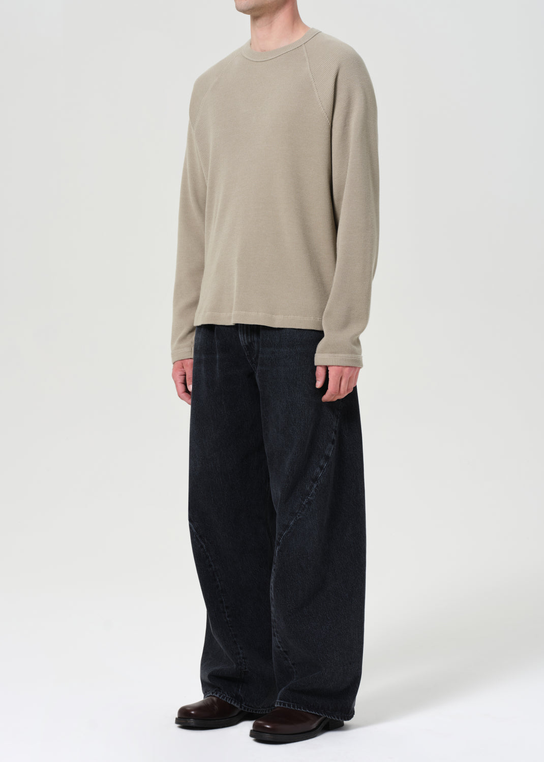 Person wearing a beige long-sleeve shirt and black pants on a white background