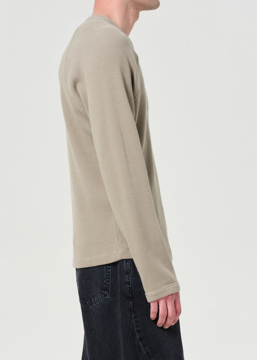 Person wearing a beige long-sleeve shirt on a plain background