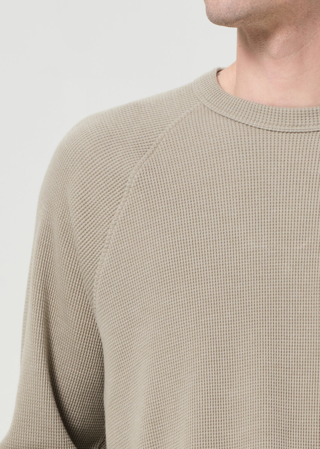 Close-up of a person wearing a beige textured sweater against a light background