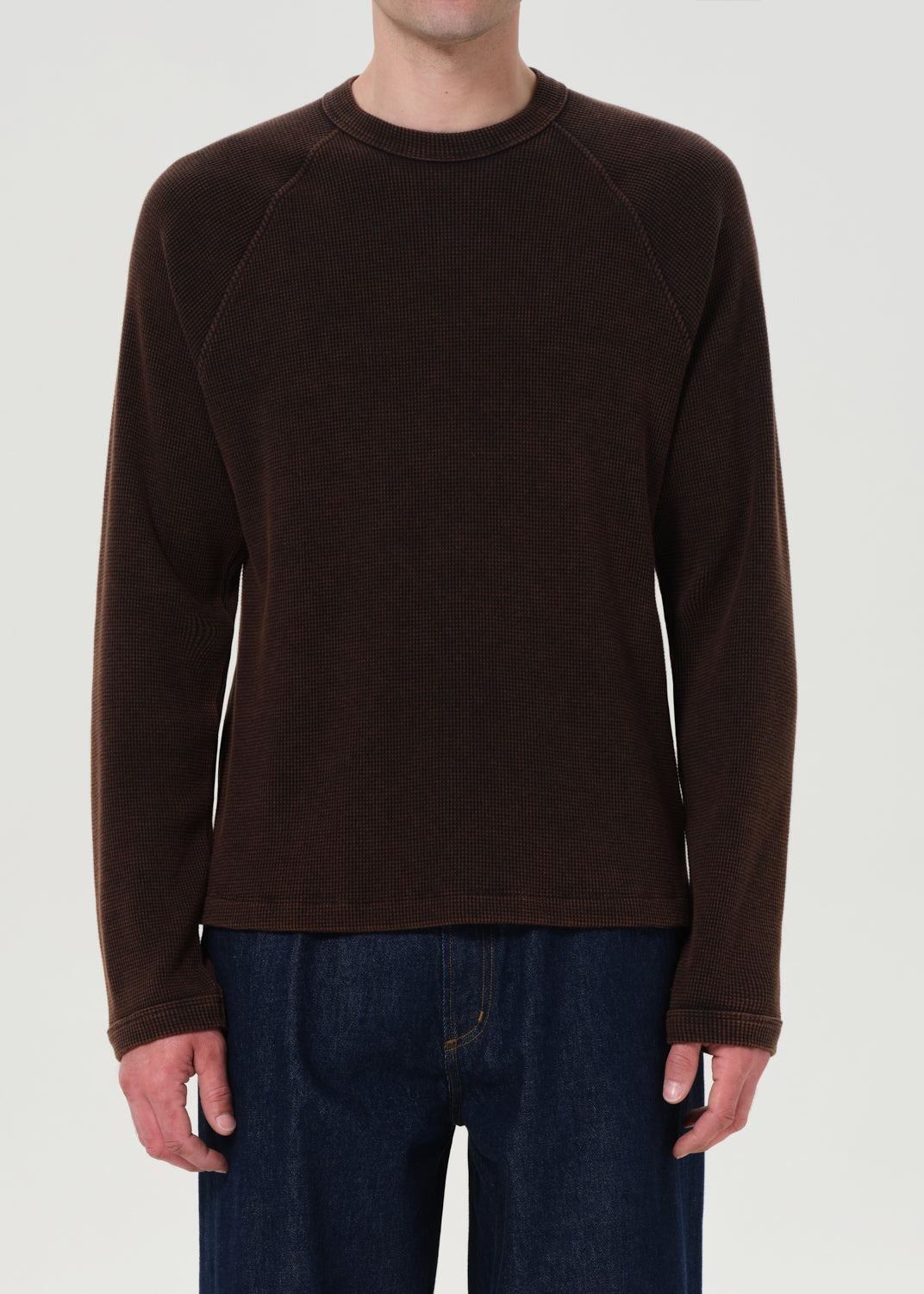 Person wearing a brown long-sleeve shirt and blue jeans on a white background