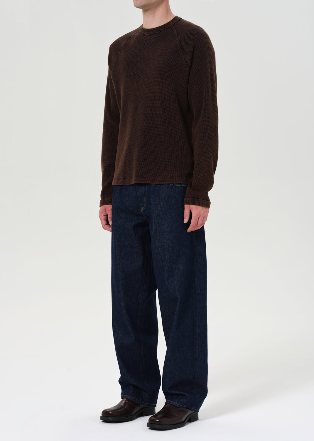 Person wearing a brown long-sleeve shirt and dark blue jeans on a white background