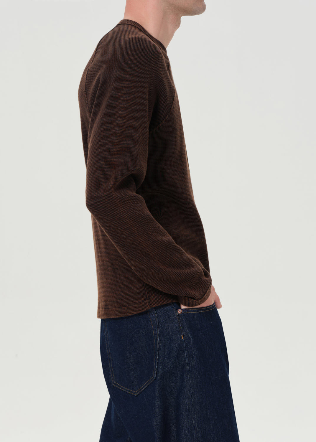 Person wearing a brown sweater and blue jeans on a light gray background