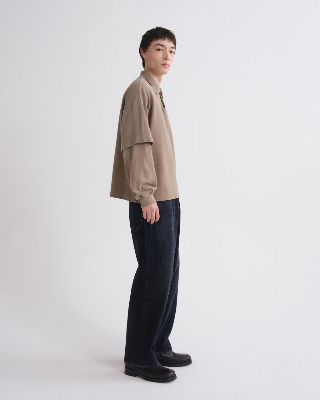 Person wearing a beige shirt and dark pants on a white background