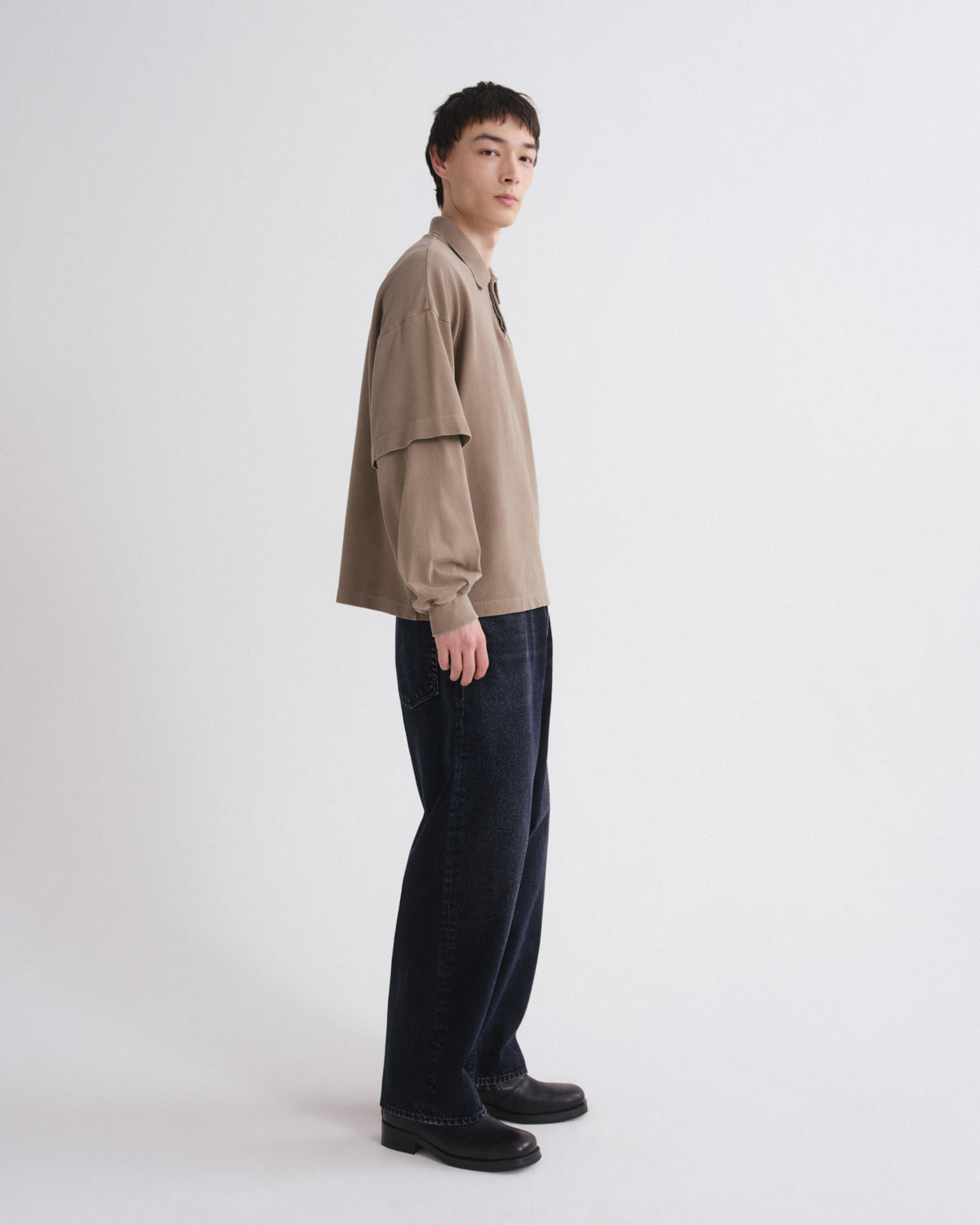 Person wearing a beige shirt and dark pants on a white background