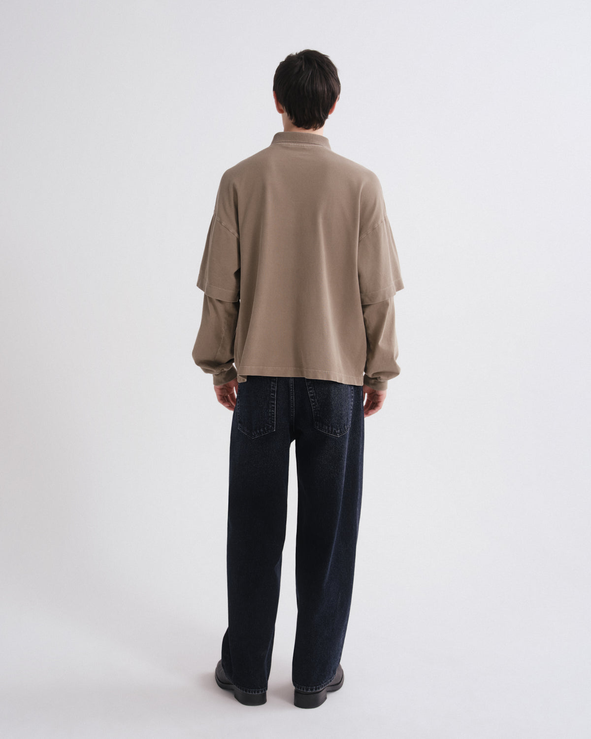 Person wearing a beige shirt and dark jeans on a white background