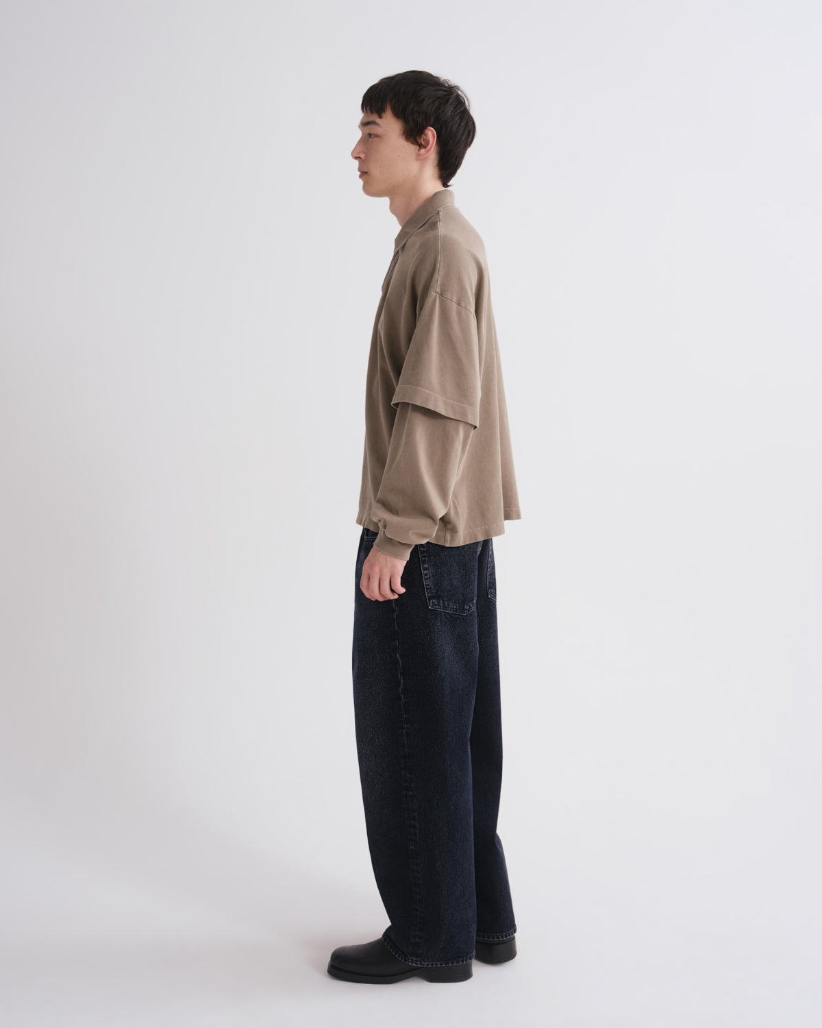 Person wearing a beige shirt and dark pants on a white background