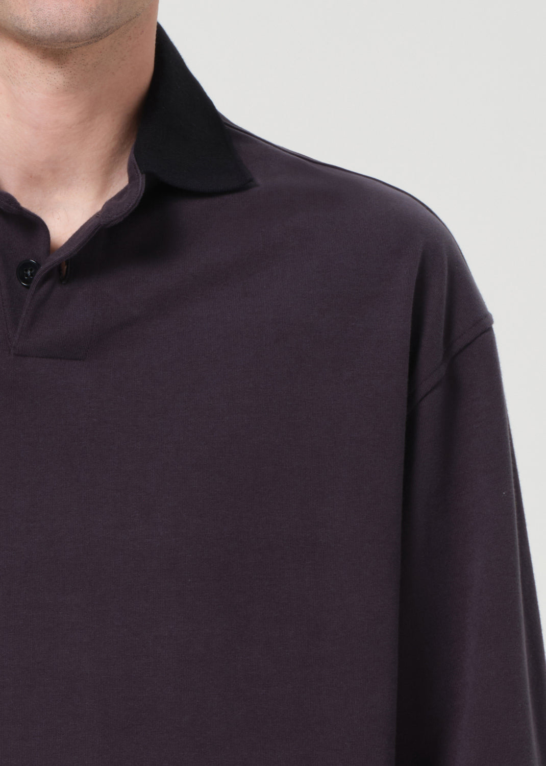Close-up of a dark purple long-sleeve polo shirt on a light gray background