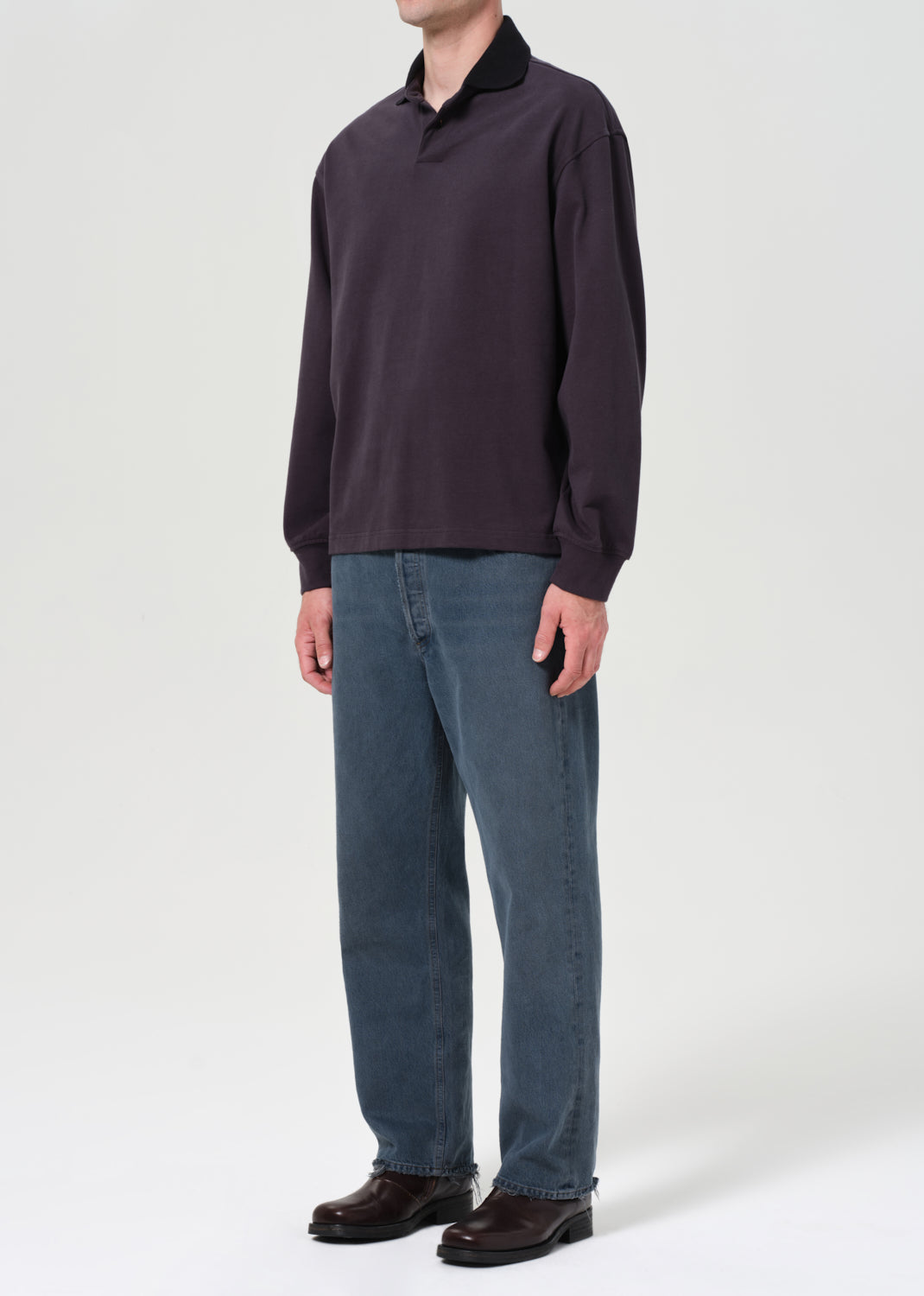 Person wearing a dark long-sleeve shirt and blue jeans on a white background