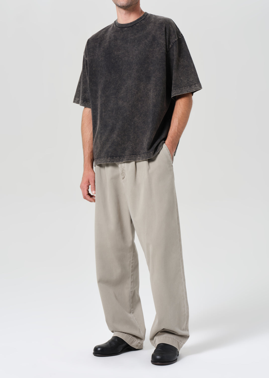 Person wearing a dark gray t-shirt and beige pants on a white background