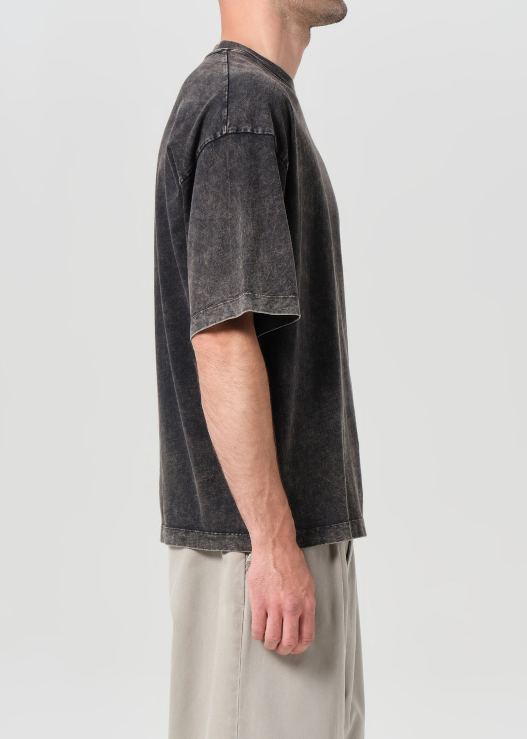 Person wearing a dark gray t-shirt and light-colored pants on a plain background