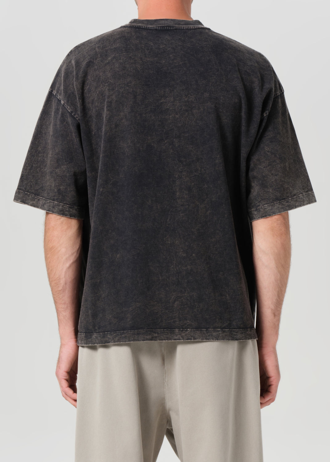 Person wearing a black distressed t-shirt and beige pants on a white background