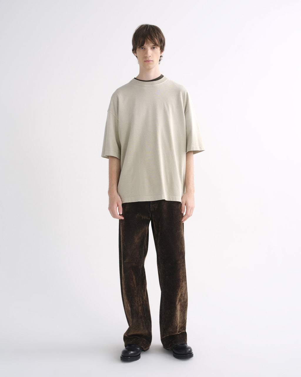 Person wearing a light beige oversized T-shirt with dark pants, front view