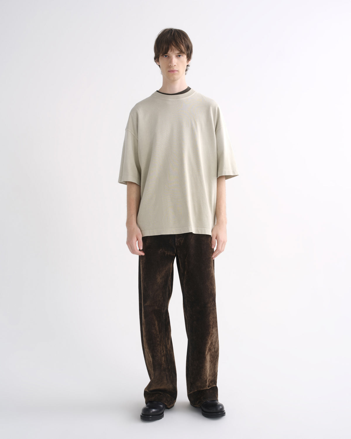 Person wearing a light beige oversized T-shirt with dark pants, front view