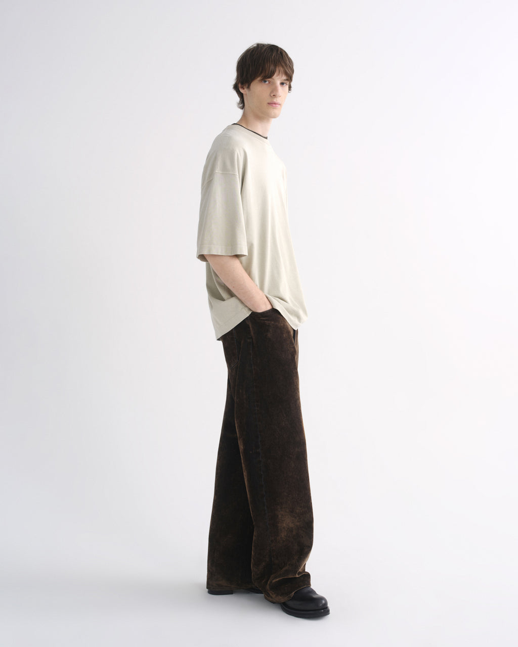 Person wearing a light beige oversized T-shirt with dark pants, side view