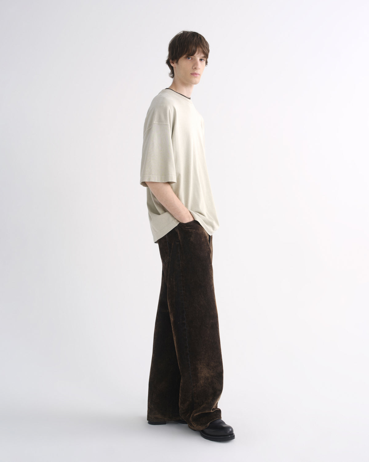 Person wearing a light beige oversized T-shirt with dark pants, side view