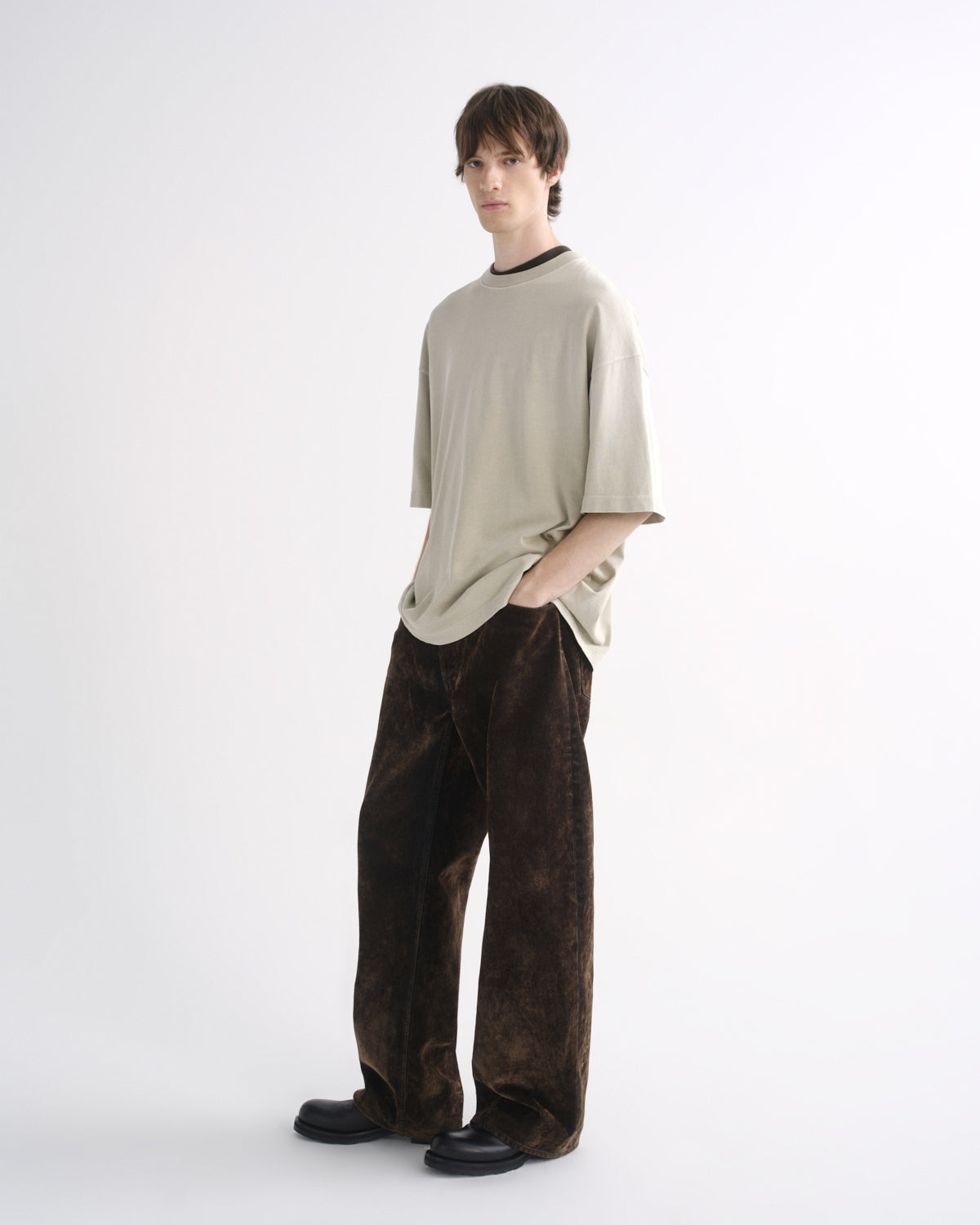 Person wearing a light beige oversized T-shirt with dark pants, opposite side view