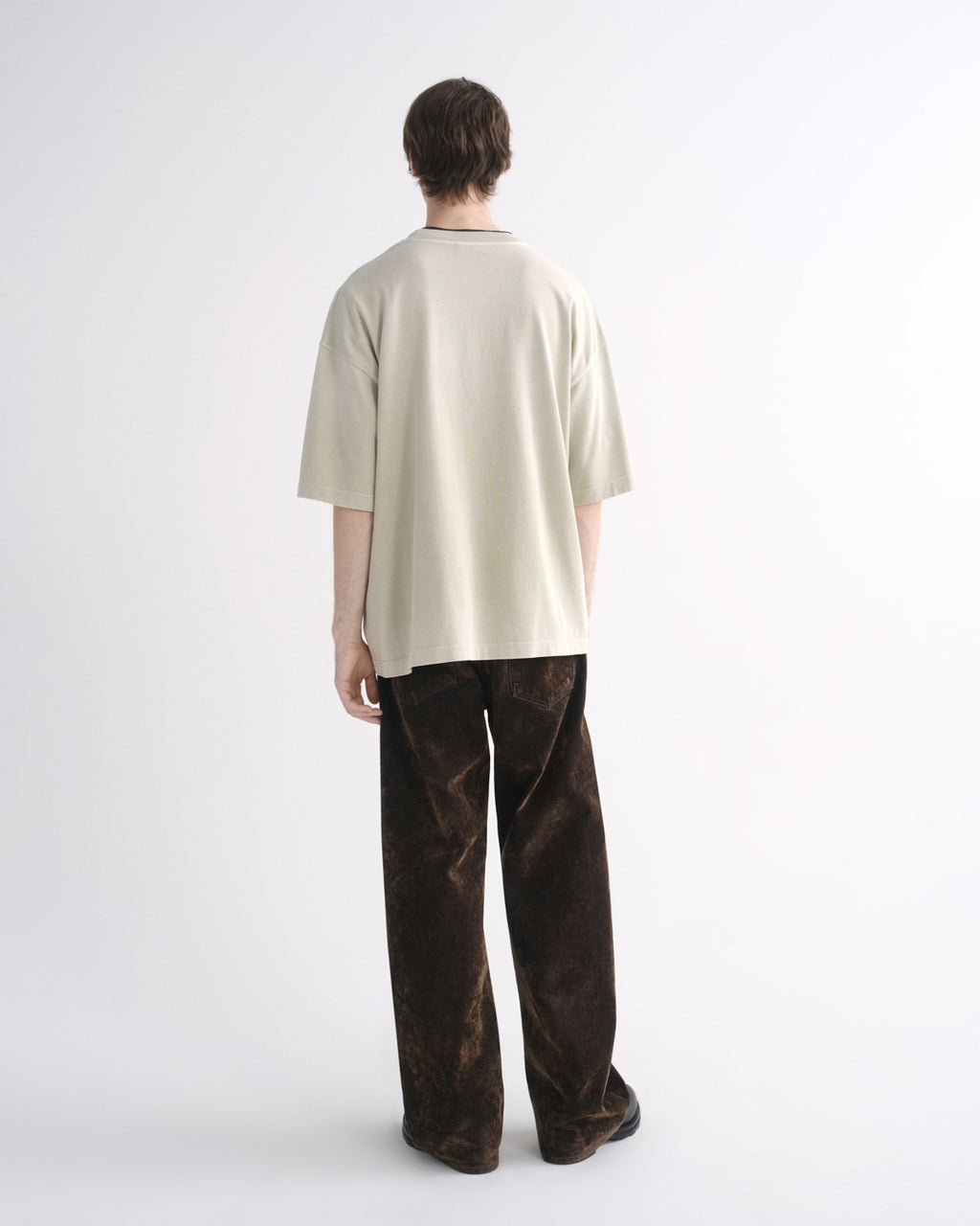 Person wearing a light beige oversized T-shirt with dark pants, back view