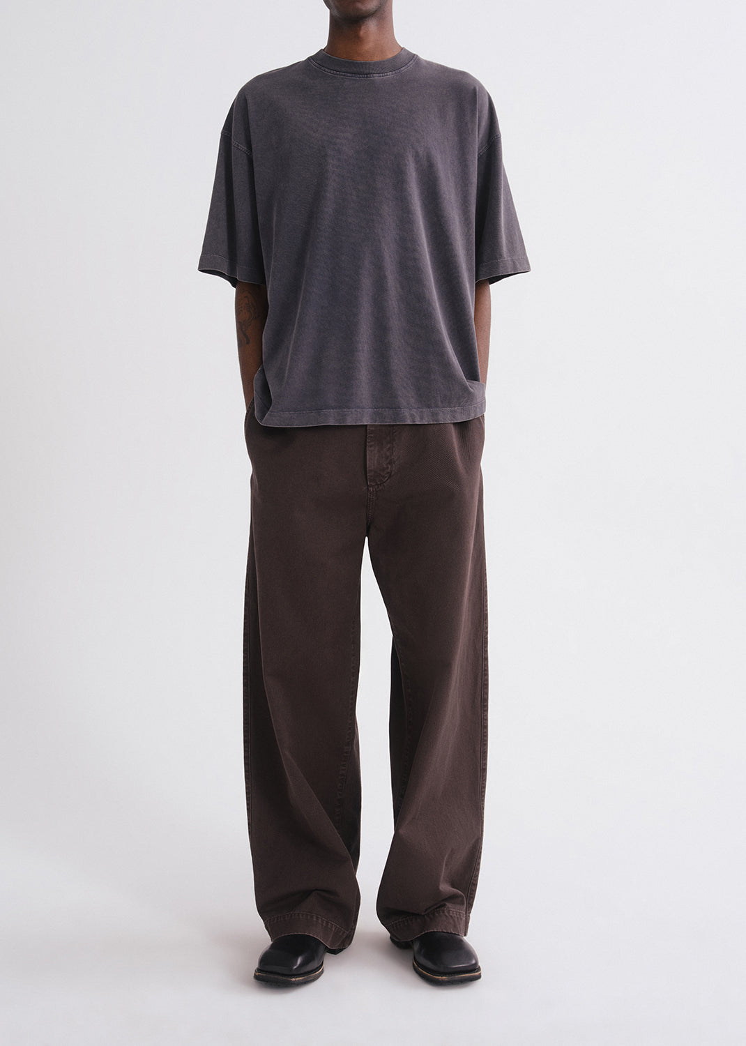 Person wearing a grey shirt and brown pants on a grey background