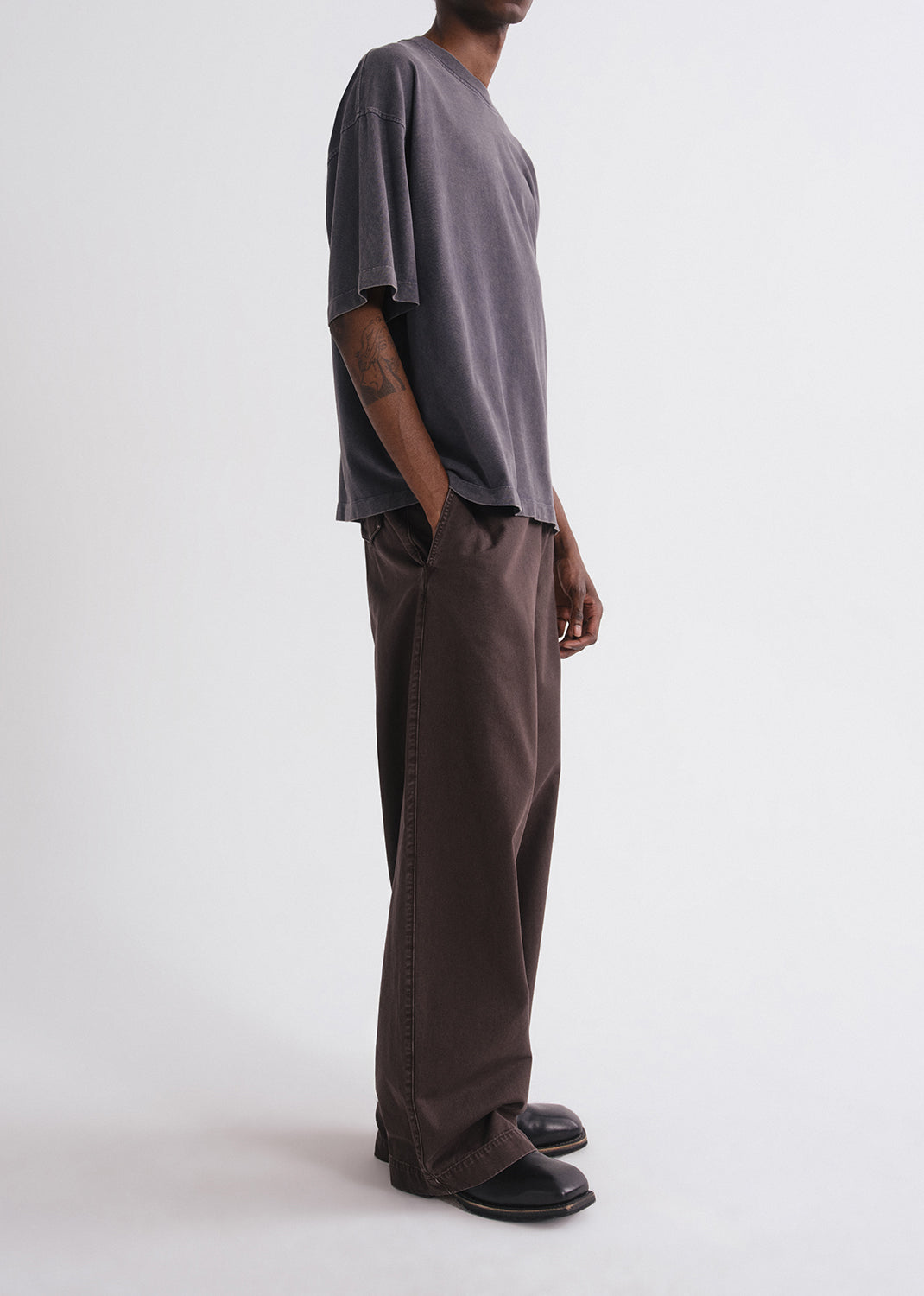 Side of person wearing a grey shirt and brown pants on a grey background