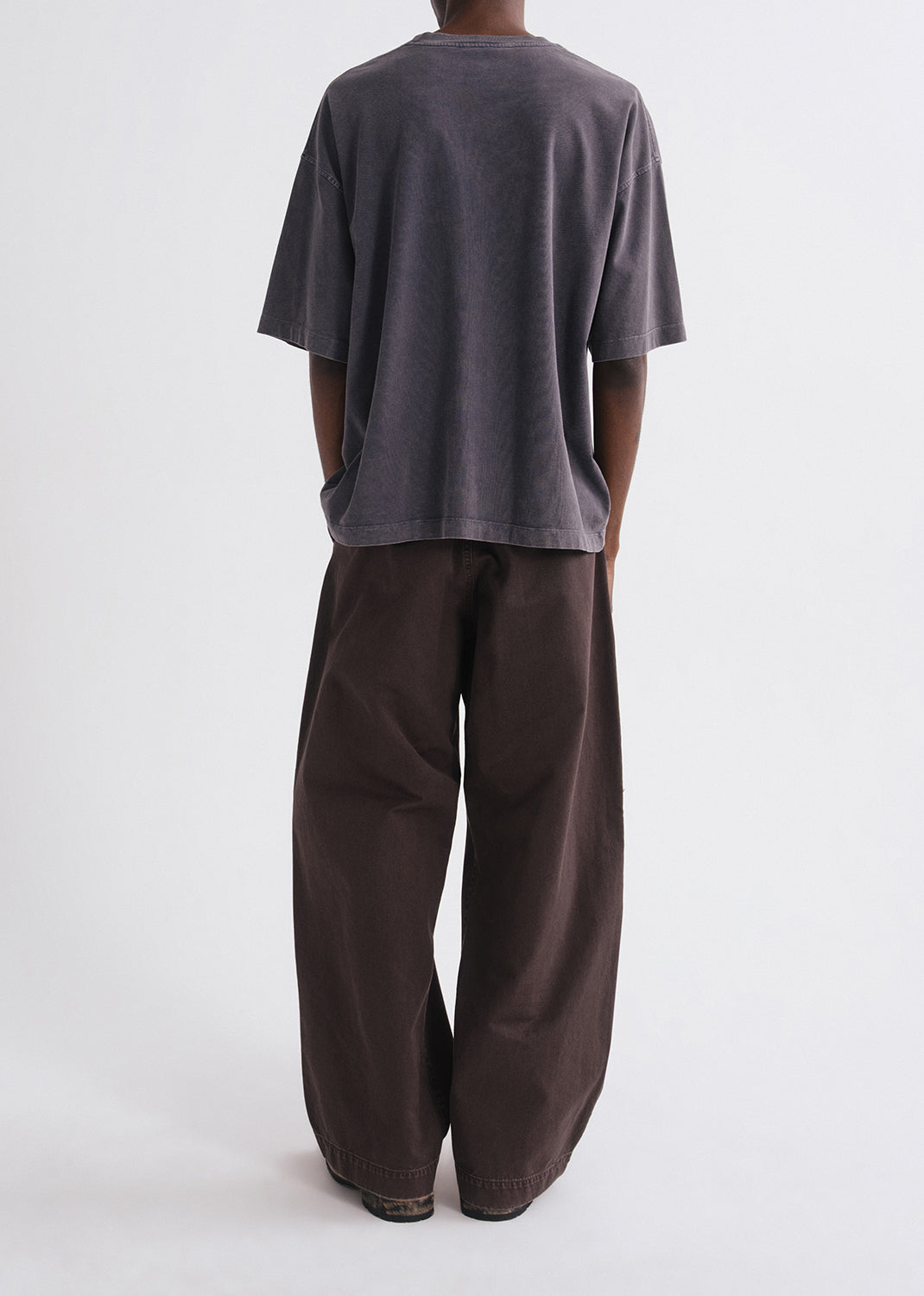 Back of person wearing a grey shirt and brown pants on a grey background