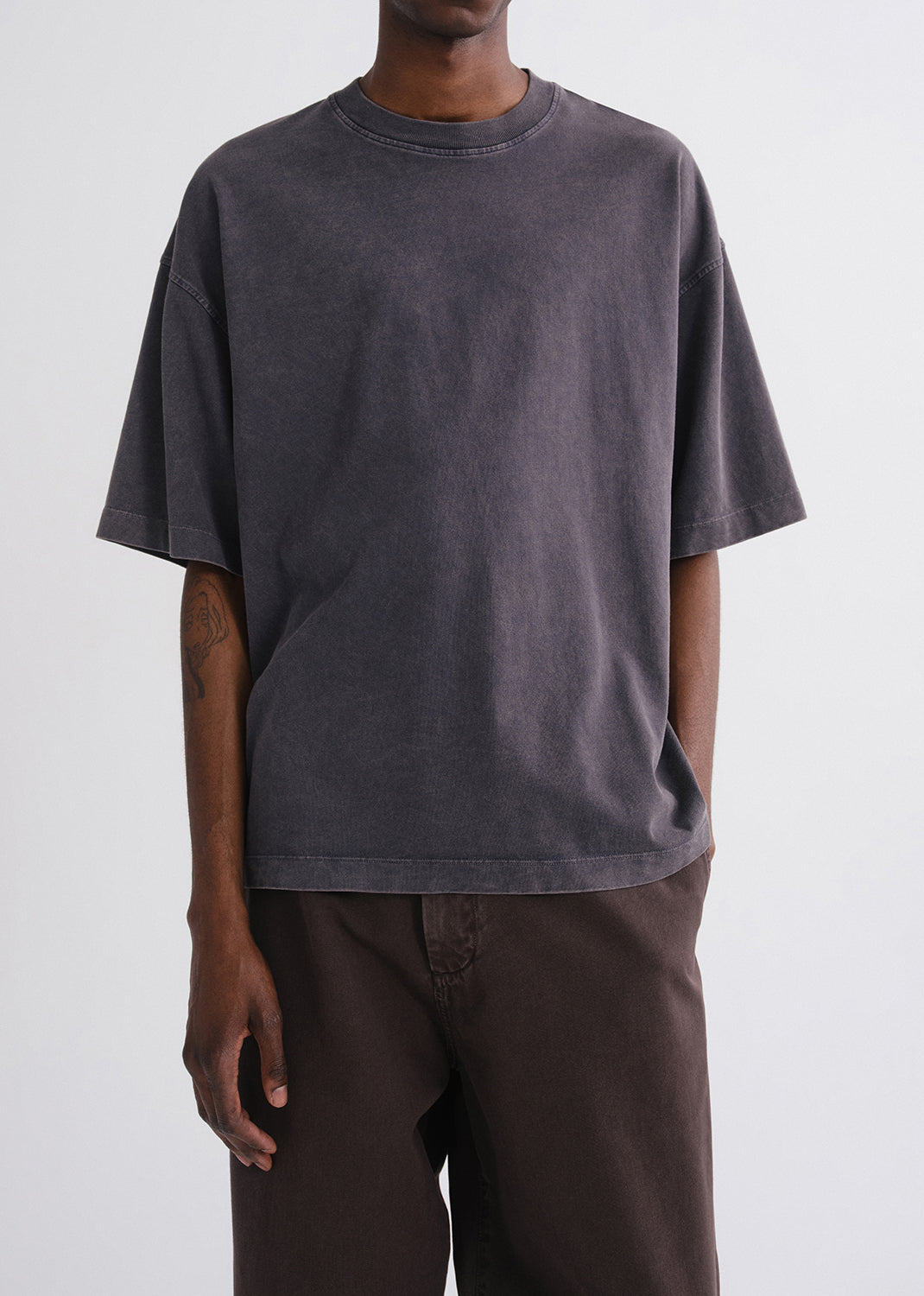 Close up of person wearing a grey shirt and brown pants on a grey background