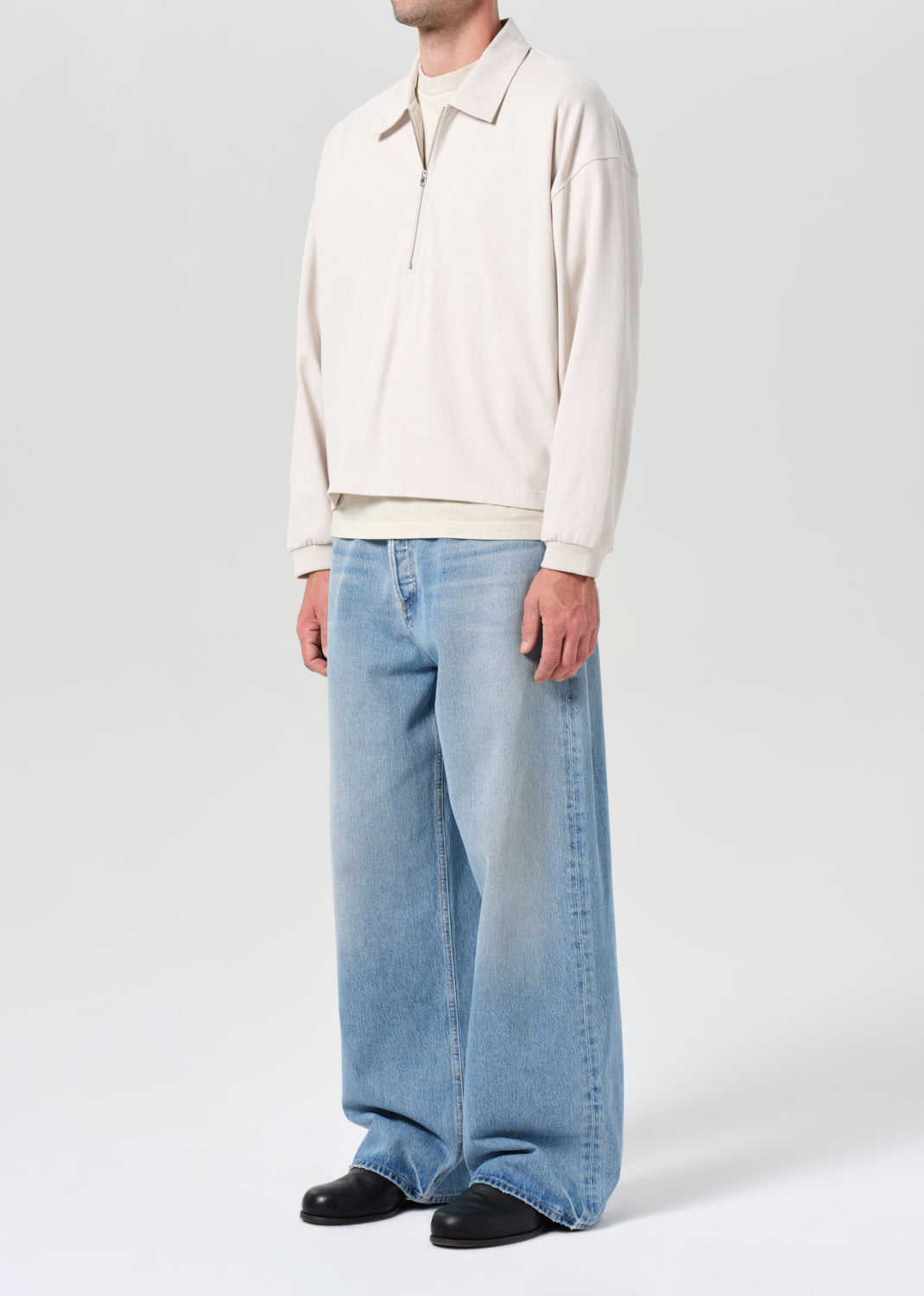 Person wearing a cream long-sleeve shirt and light blue jeans on a white background