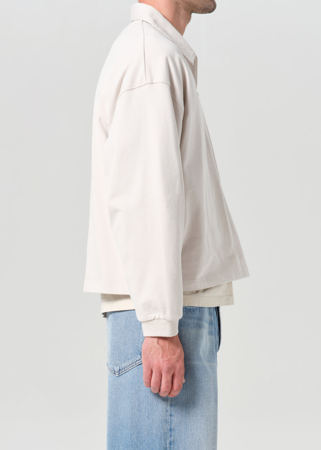 Person wearing a light-colored shirt and jeans on a plain background