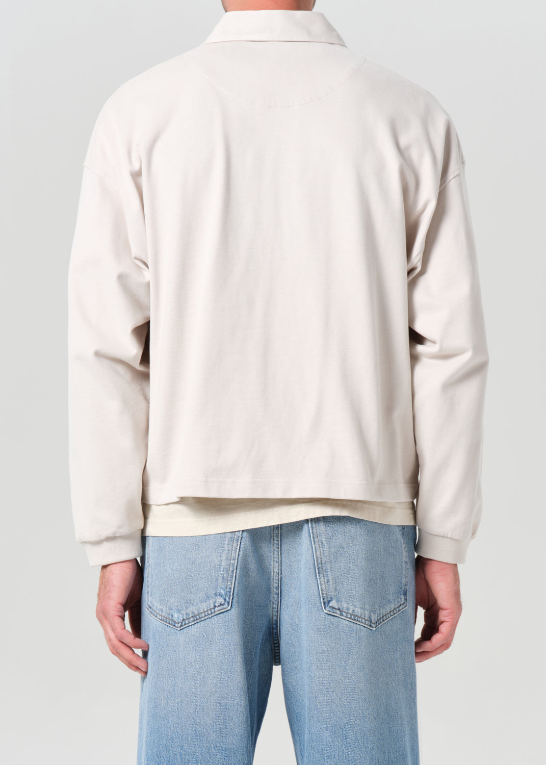 Person wearing a beige sweater and light blue jeans on a plain background