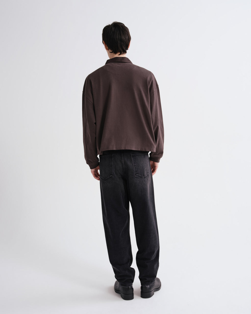 Person wearing a brown sweater and black pants on a grey background