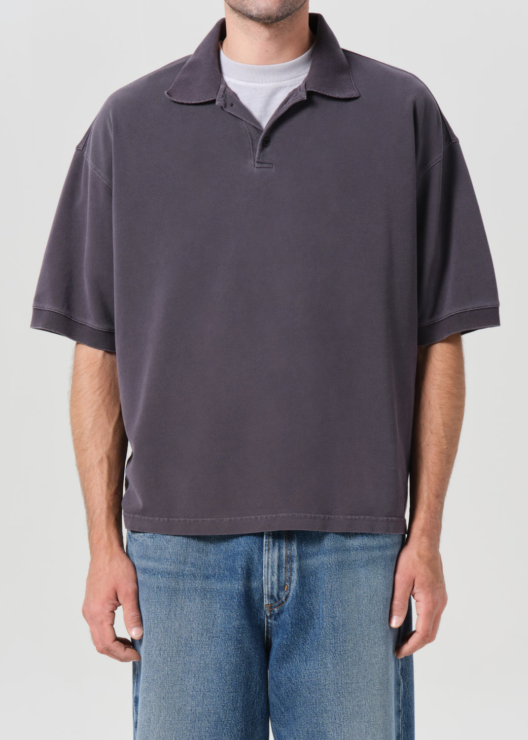 Person wearing a dark gray polo shirt and blue jeans on a light gray background