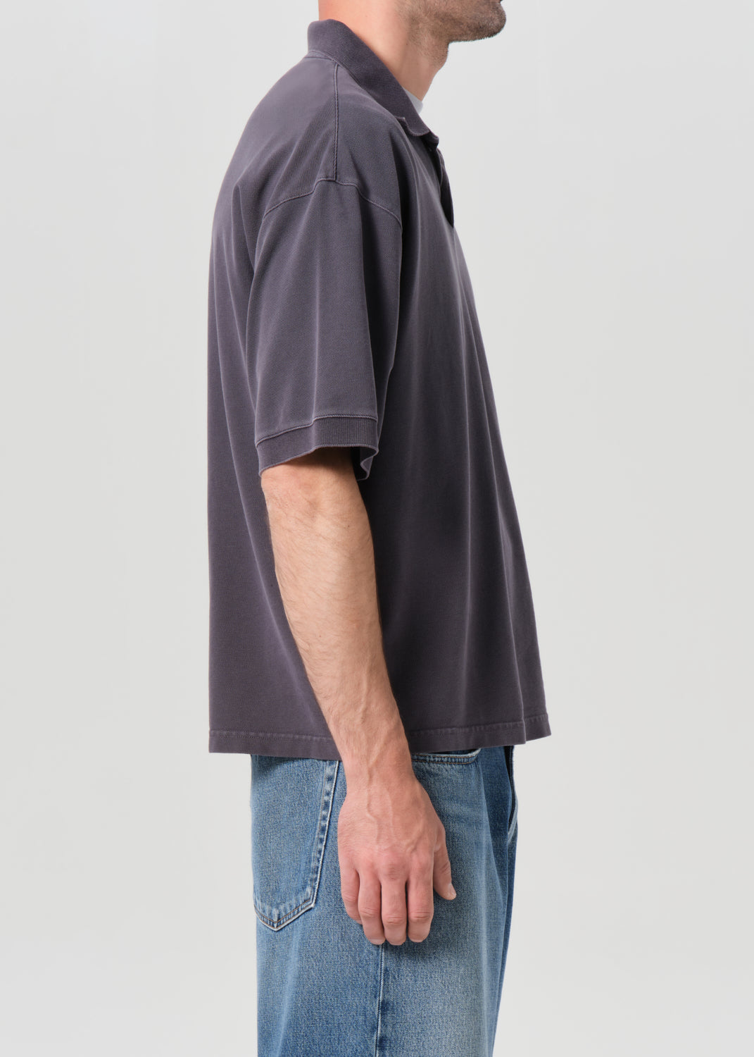 Person wearing a dark gray polo shirt and blue jeans on a light gray background