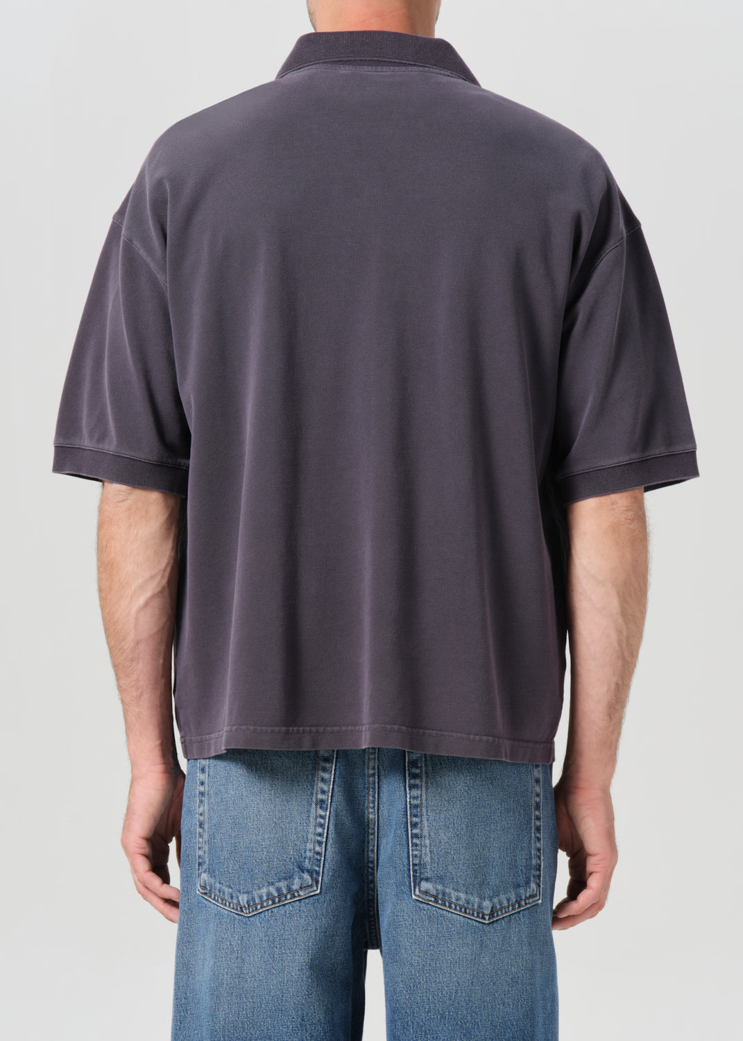 Person wearing a dark gray polo shirt and blue jeans on a light gray background