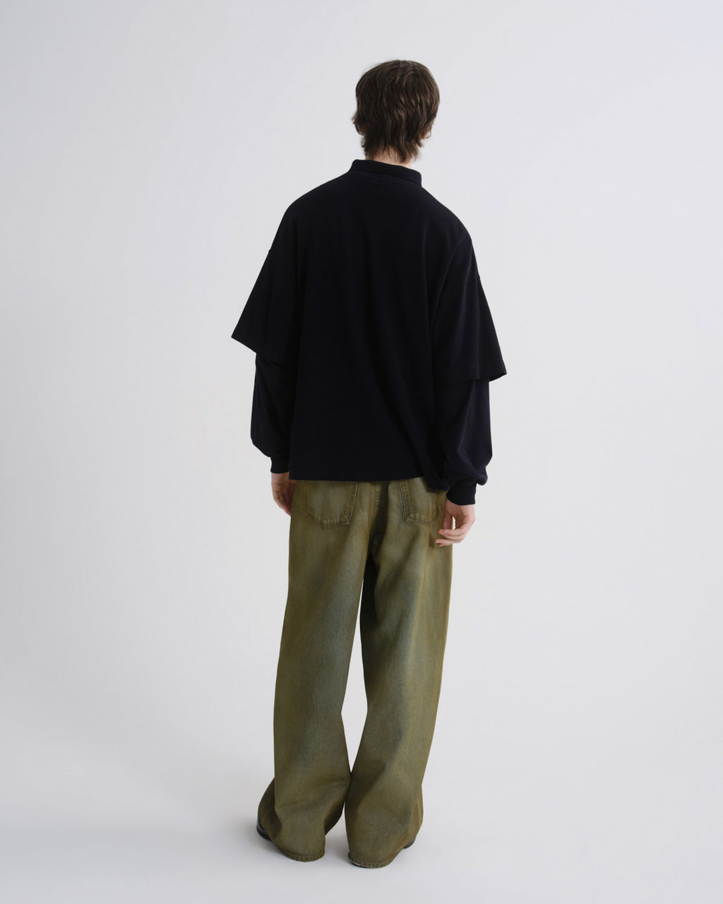 Person wearing a black jacket and green pants on a white background
