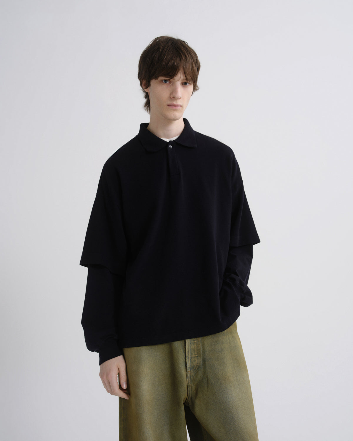 Person wearing a black oversized sweater and green pants on a plain background