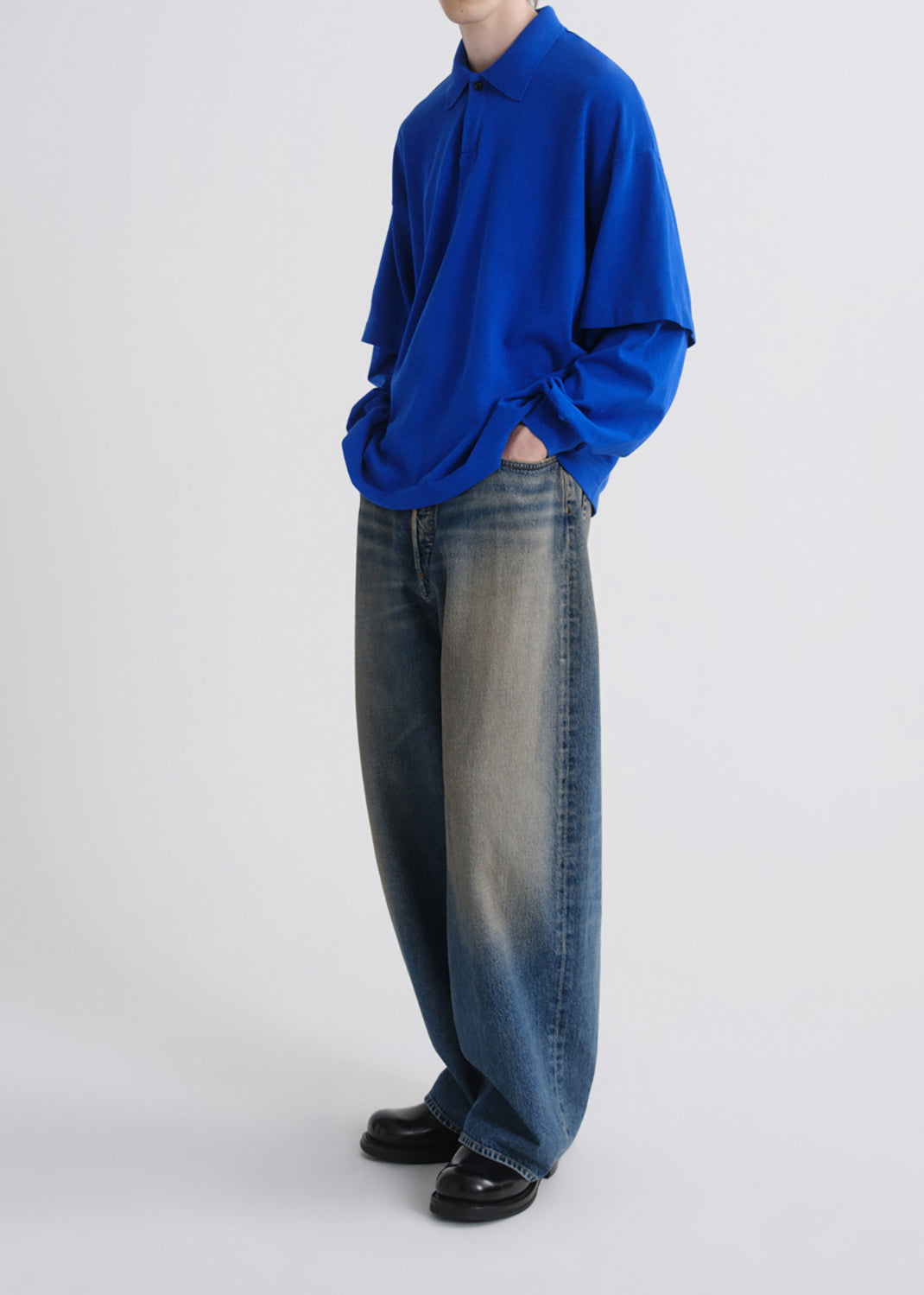 A model wearing a vibrant royal blue long-sleeve collared shirt and wide-leg faded blue jeans, standing against a grey background.