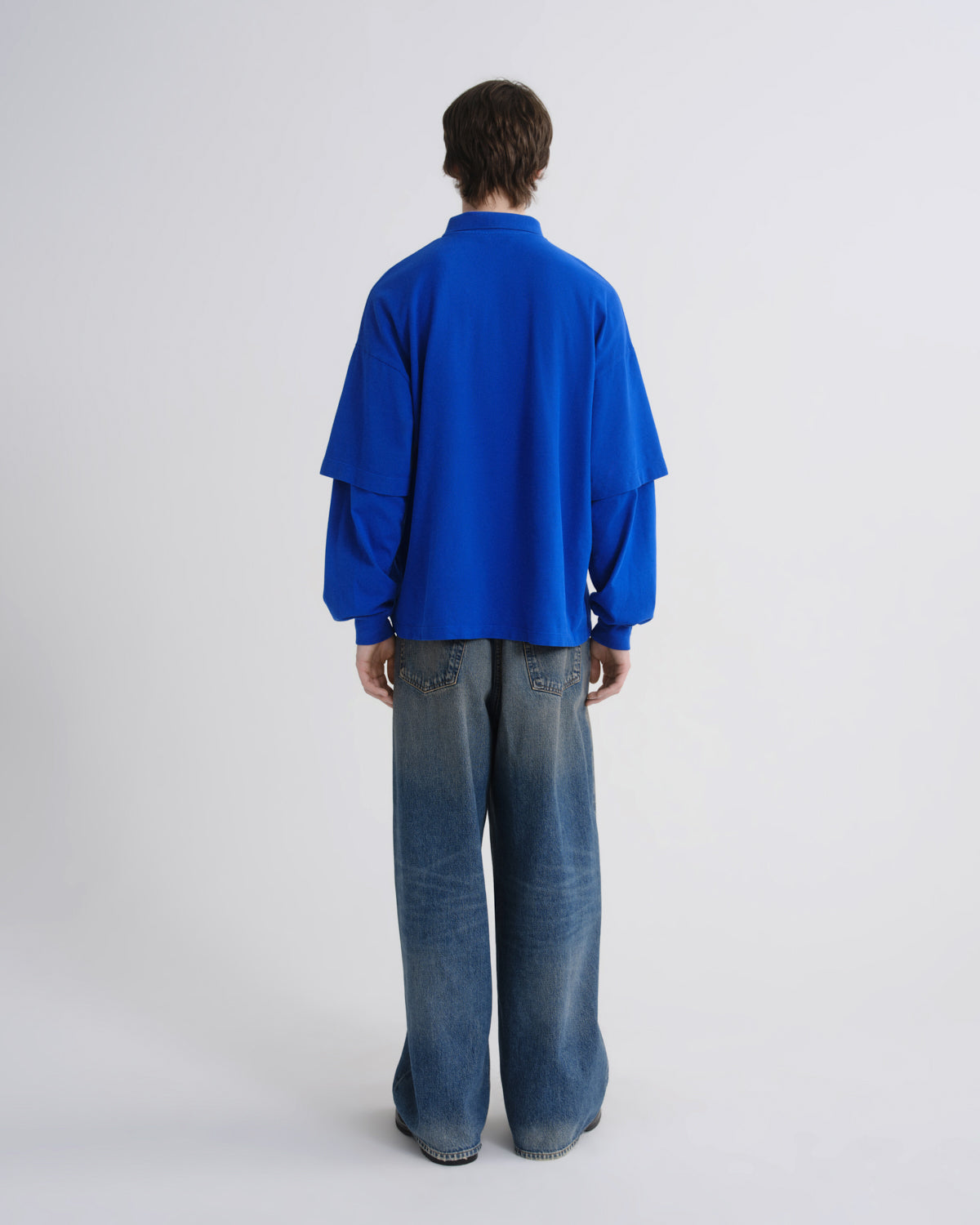 Person wearing a blue oversized shirt and jeans on a white background