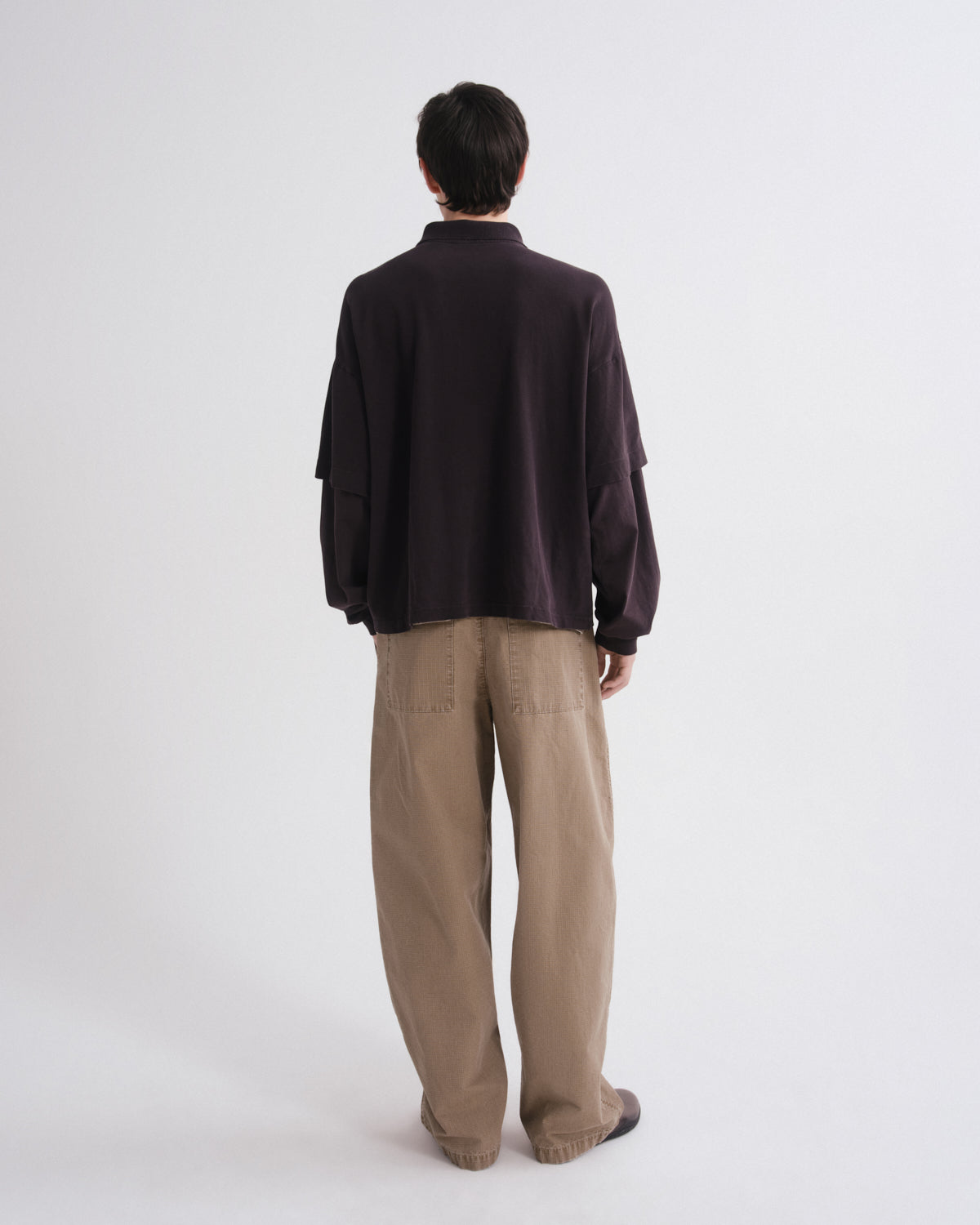 Person wearing a dark brown sweater and beige pants on a white background