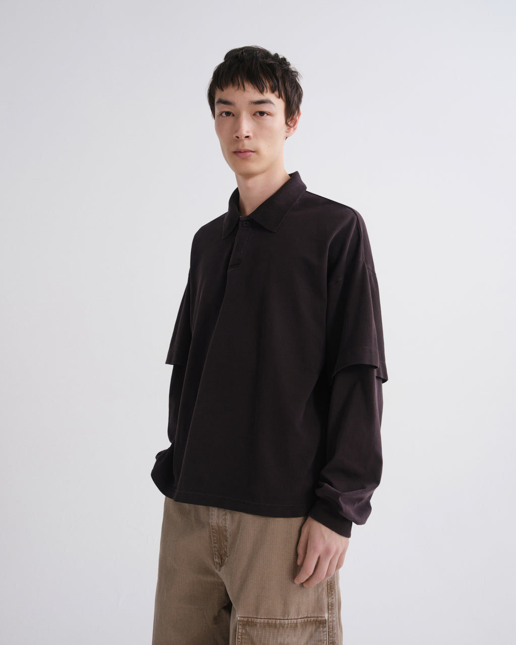 Person wearing a dark brown shirt and beige pants on a white background