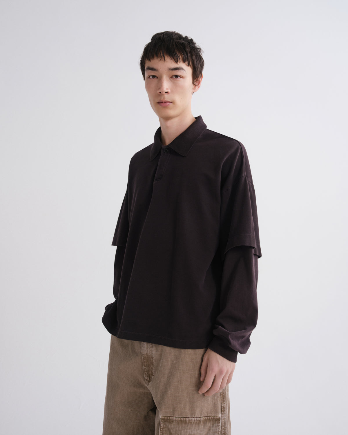 Person wearing a dark brown shirt and beige pants on a white background