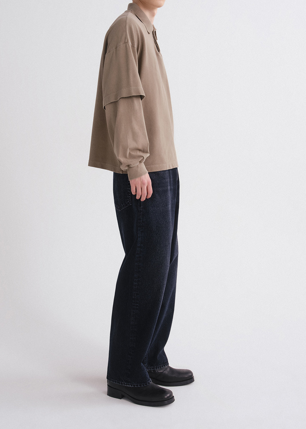 Person wearing a beige shirt and dark jeans on a white background