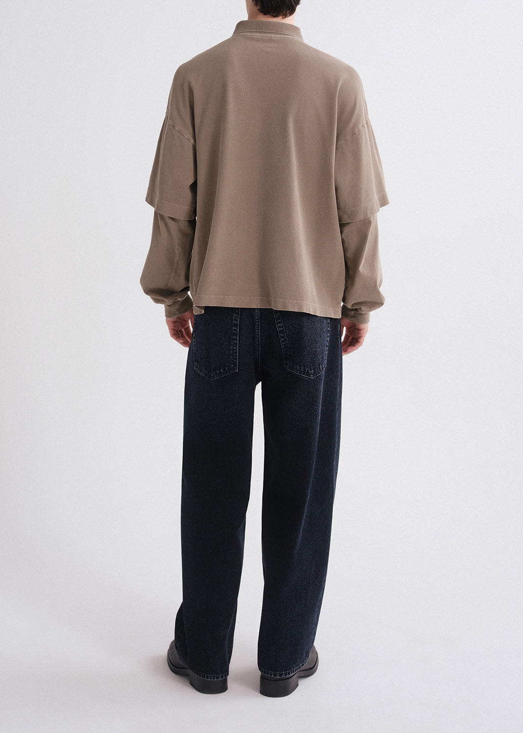 Person wearing a beige shirt and dark jeans on a white background
