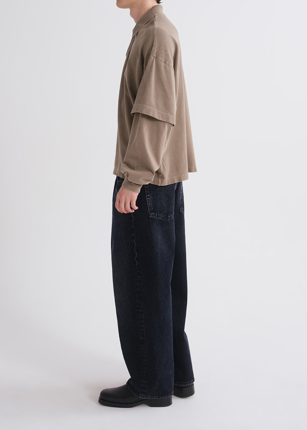 Person wearing a beige shirt and dark jeans on a white background