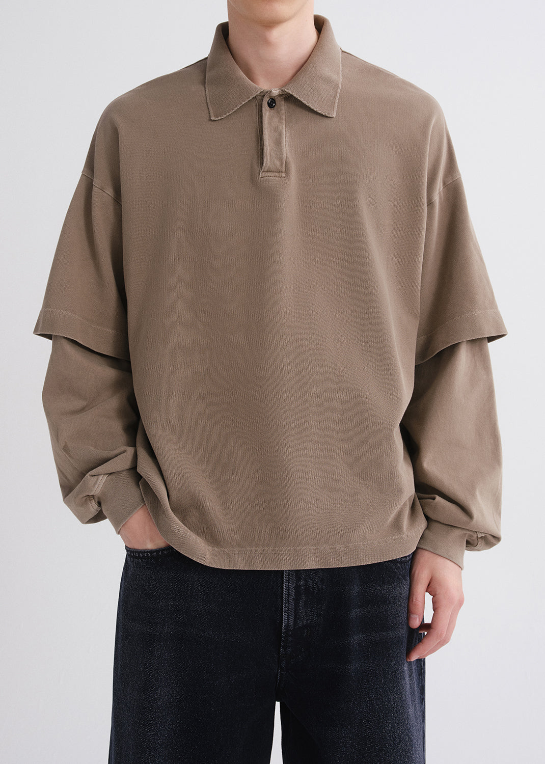 Person wearing a brown oversized shirt with a plain background